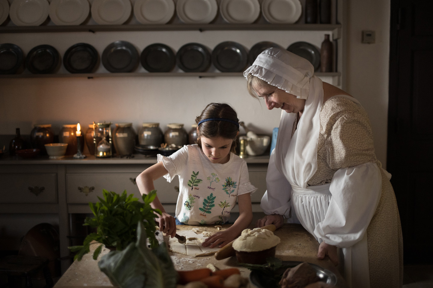 A child learns traditional baking skills from a heritage interpreter in a historic Georgian kitchen.