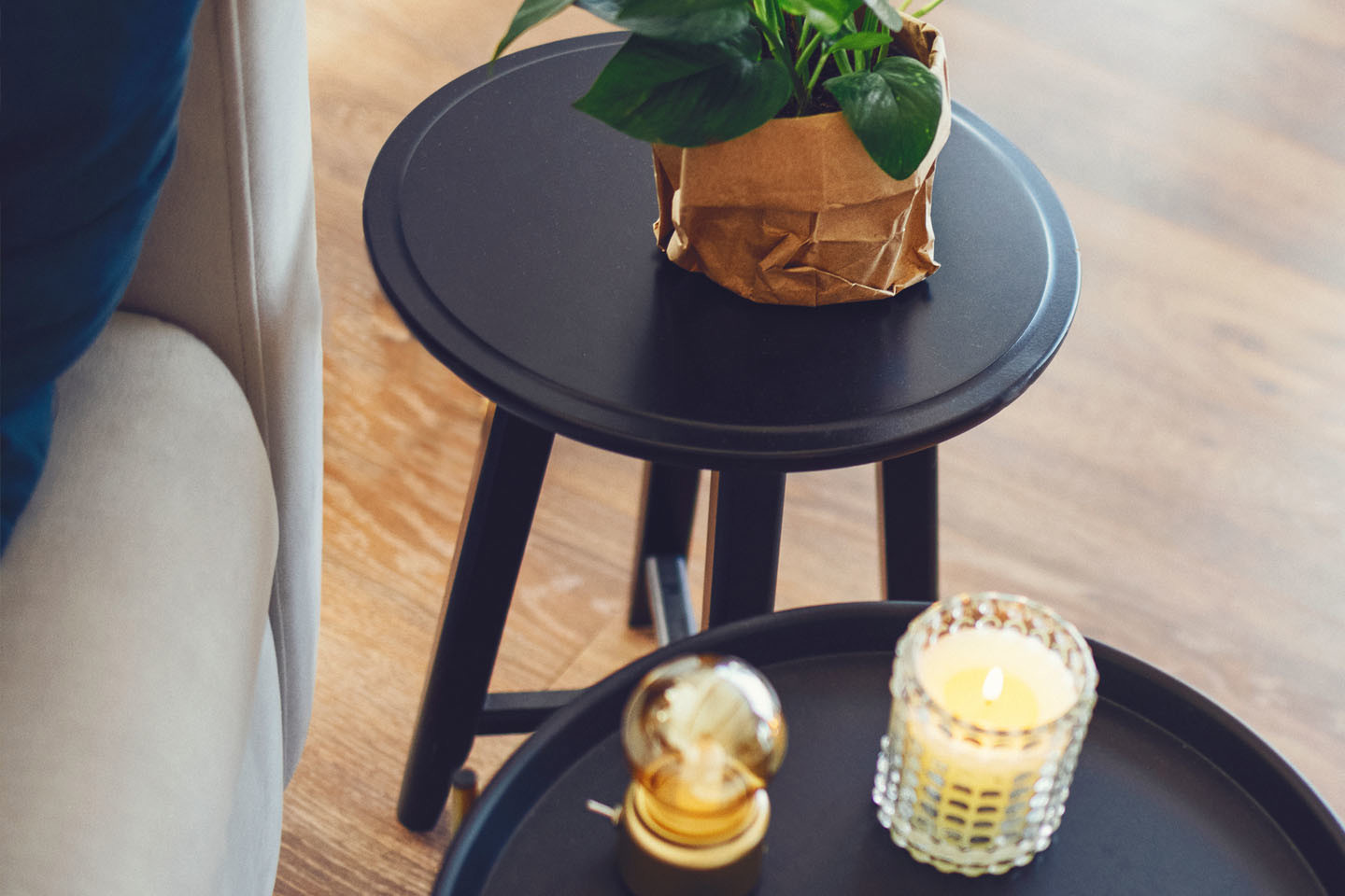 two side tables; one with a plant in brown paper bag and the other with a light and a lit candle