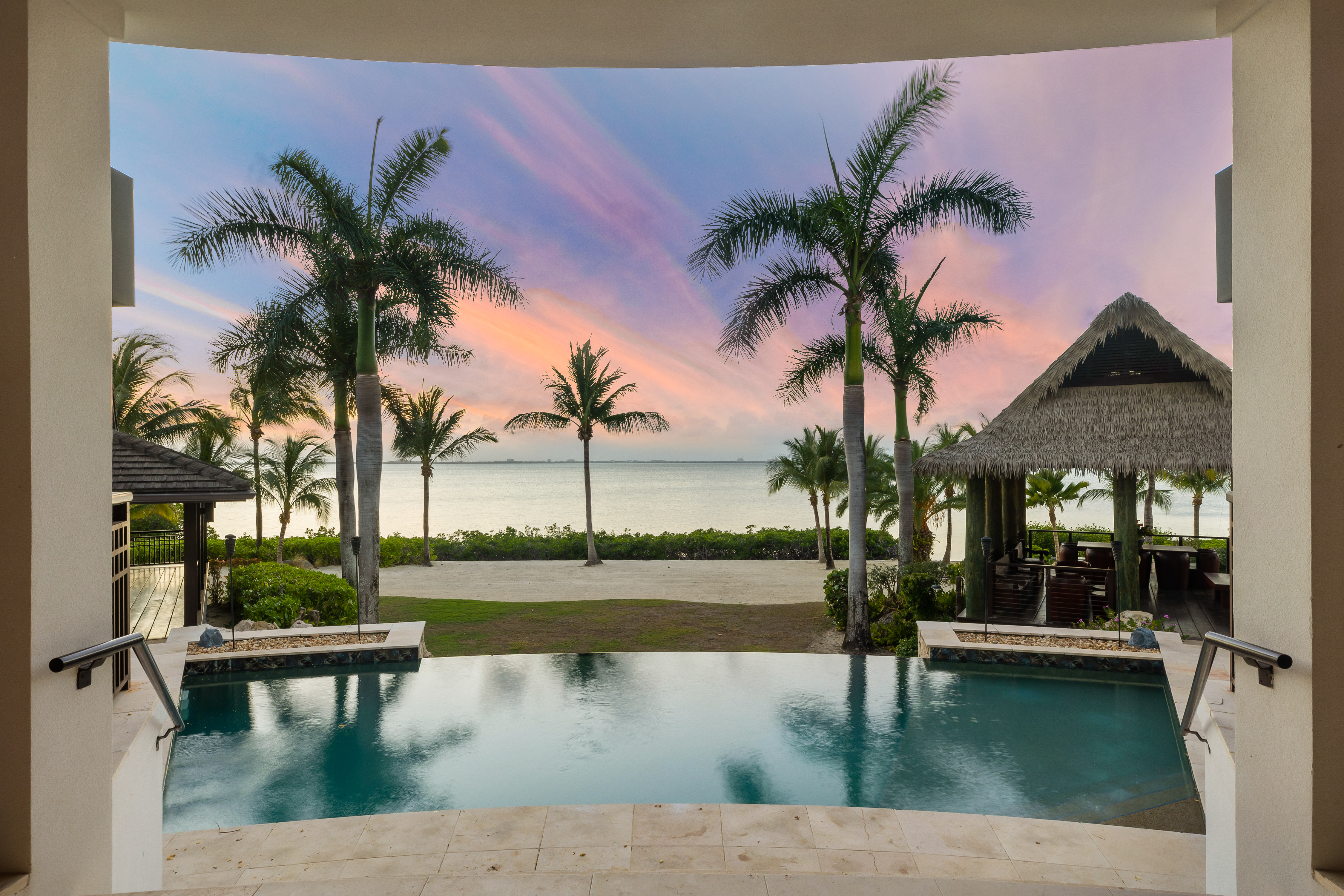 Outside view of pool with straw hut outside and palm trees