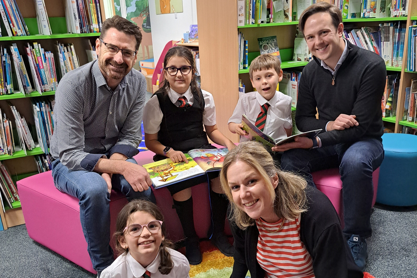 adults and children reading together in a primary school library, supporting Ogier and Every Child Our Future literacy partnership in Jersey.